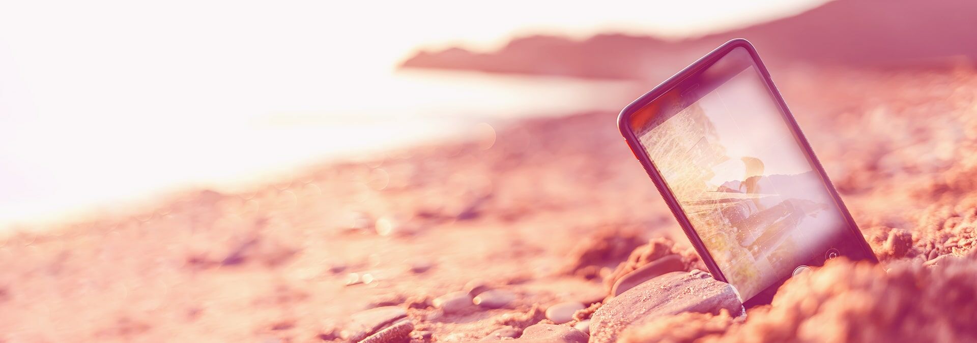 Handy, welches im Sand steckt und im Hintergrund ist das Meer zu sehen